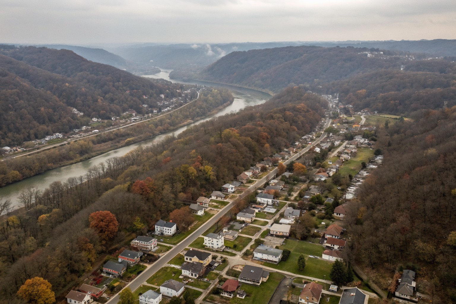 Aerial view of hillside rows of older houses beside a wooded river valley