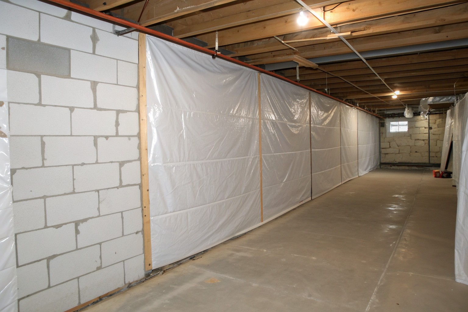 White reinforced plastic sheeting taped at the seams over a block basement wall